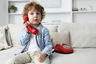 Photo of Cute little boy with telephone on sofa indoors