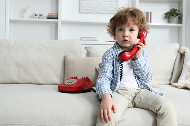 Photo of Cute little boy with telephone on sofa indoors