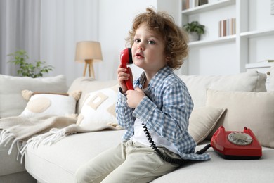 Photo of Cute little boy with telephone on sofa indoors