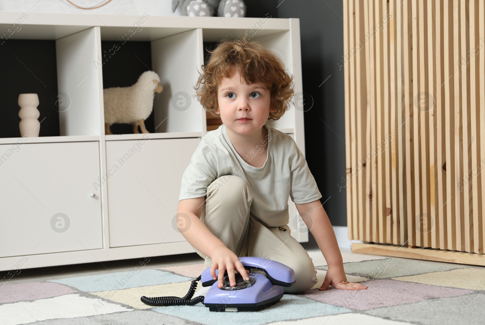 Photo of Cute little boy with telephone on floor indoors