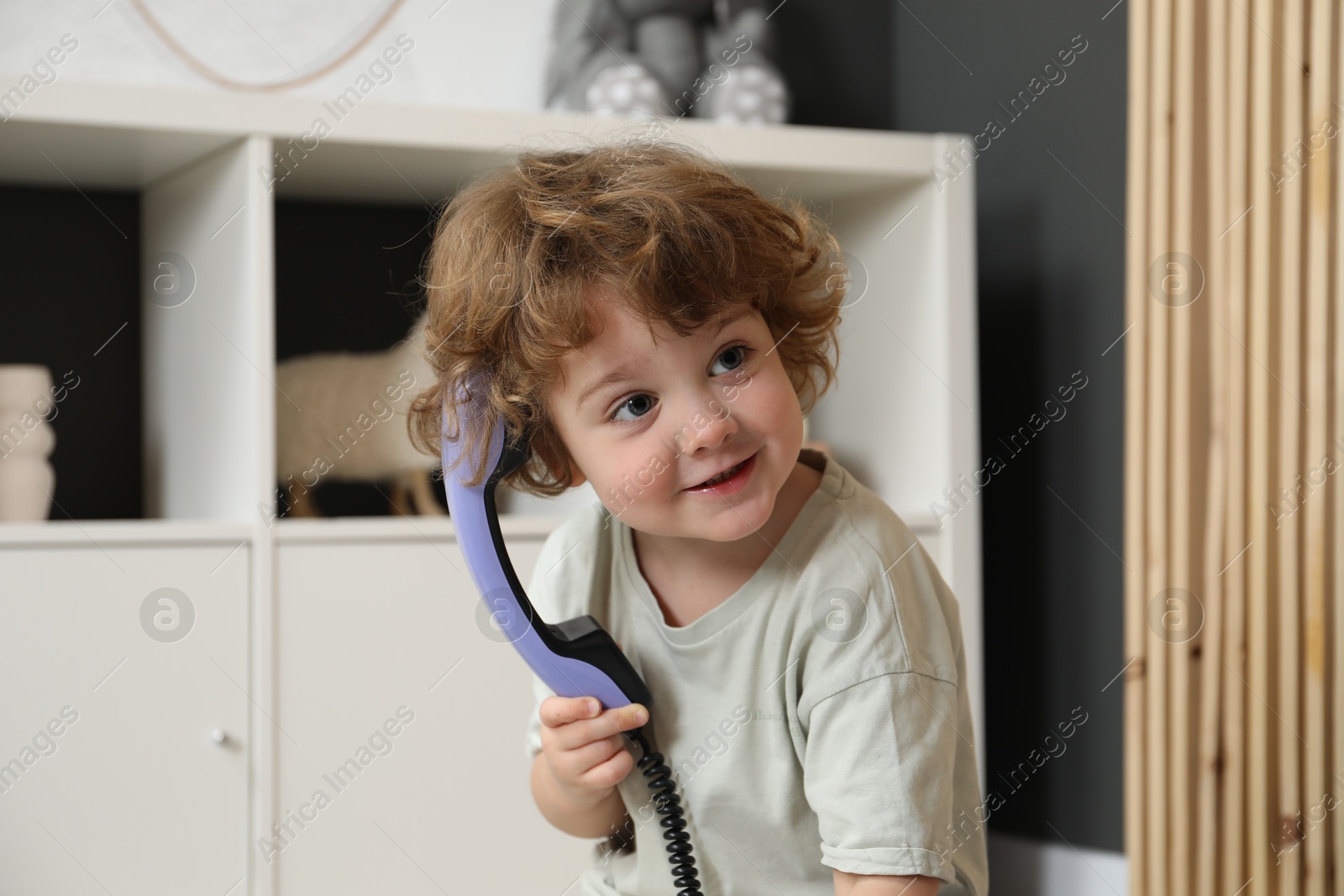 Photo of Cute little boy with telephone handset indoors