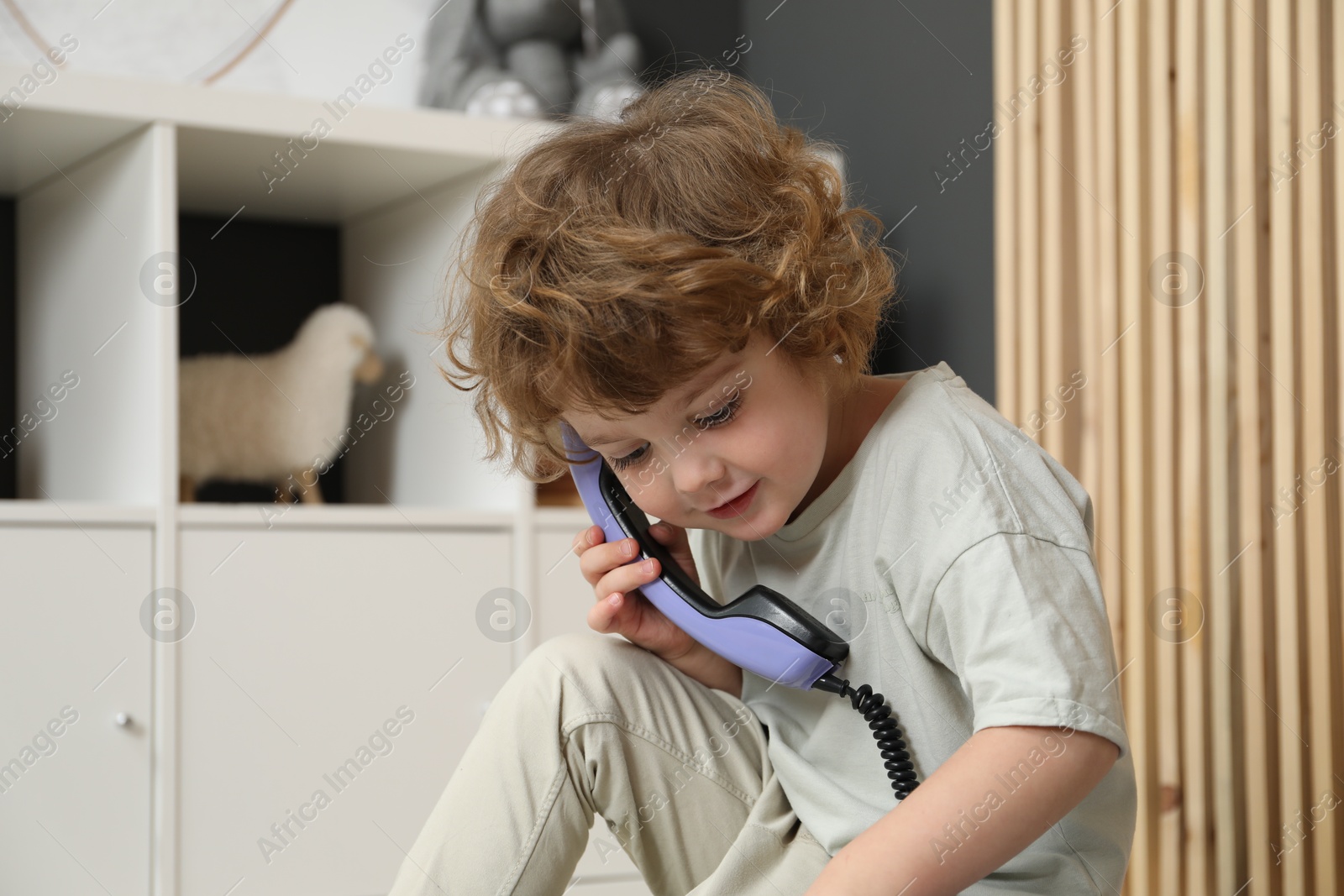 Photo of Cute little boy with telephone handset indoors