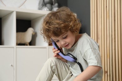 Photo of Cute little boy with telephone handset indoors