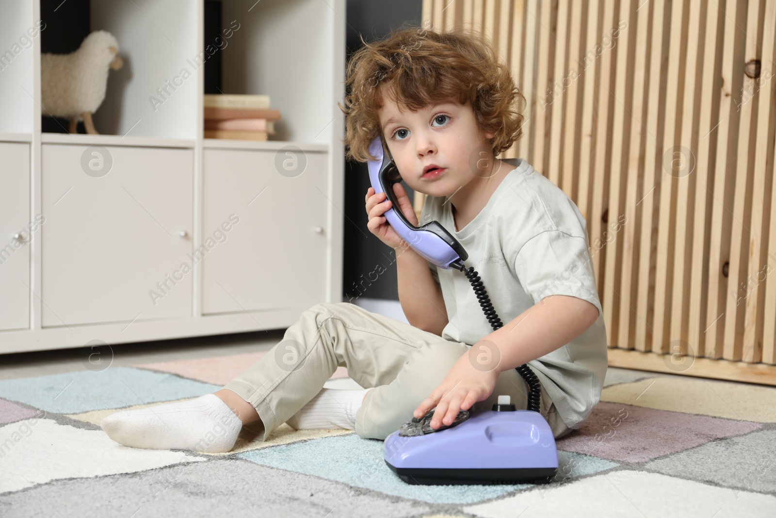 Photo of Cute little boy with telephone on floor indoors