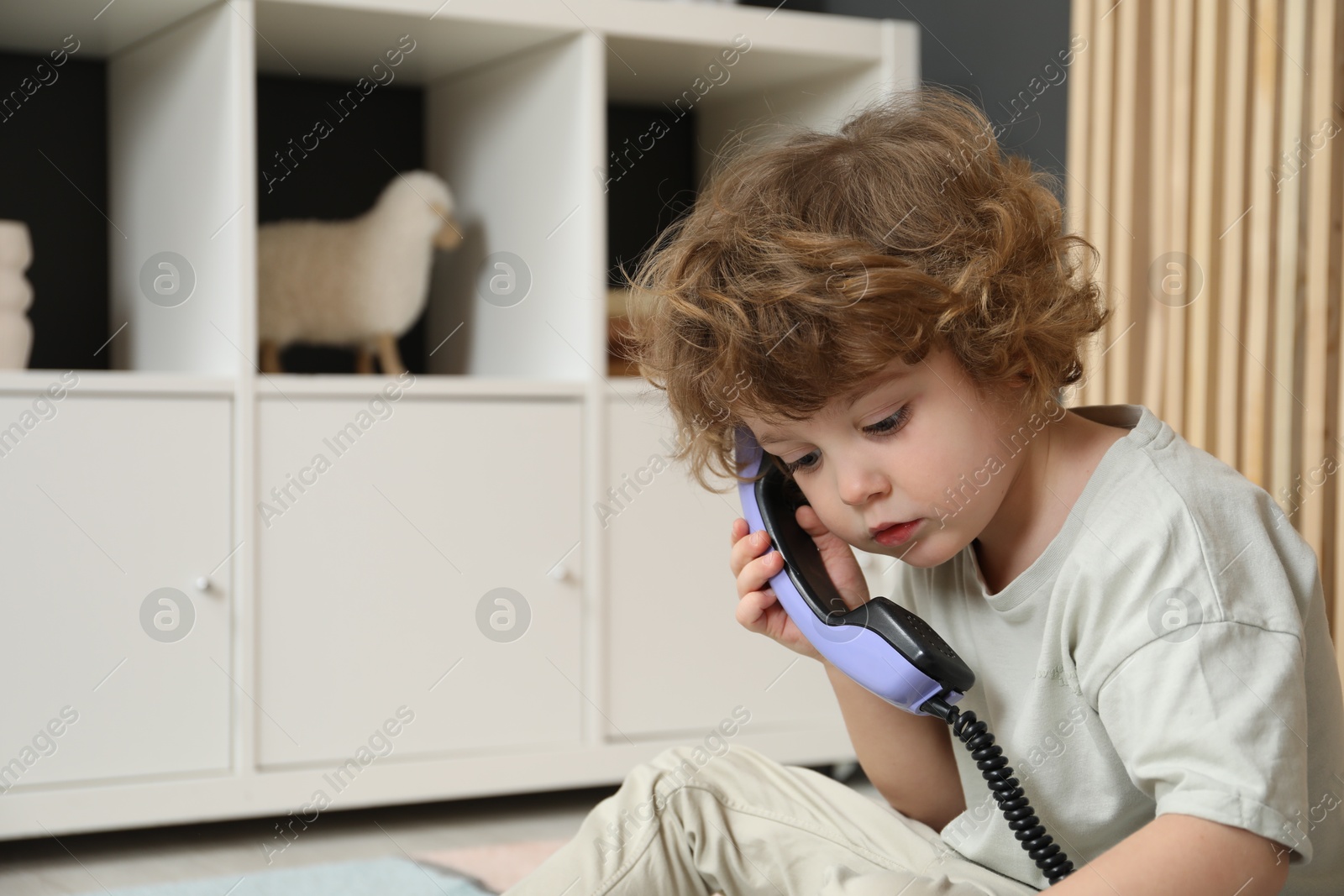 Photo of Cute little boy with telephone handset on floor indoors, space for text