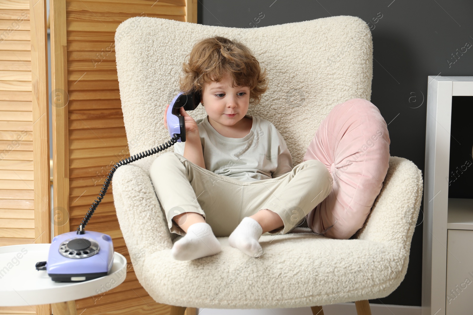 Photo of Cute little boy with telephone in armchair indoors