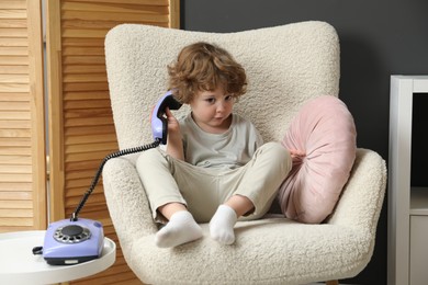 Photo of Cute little boy with telephone in armchair indoors