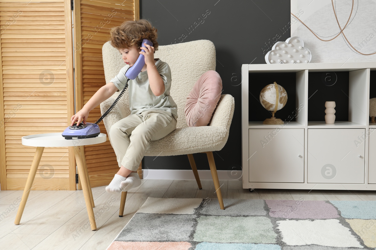 Photo of Cute little boy with telephone in armchair indoors