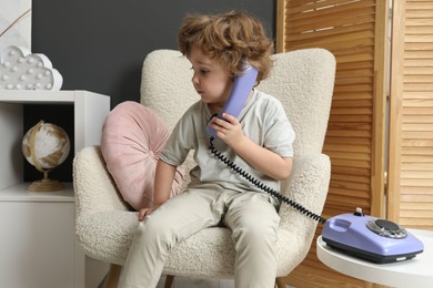 Photo of Cute little boy with telephone in armchair indoors