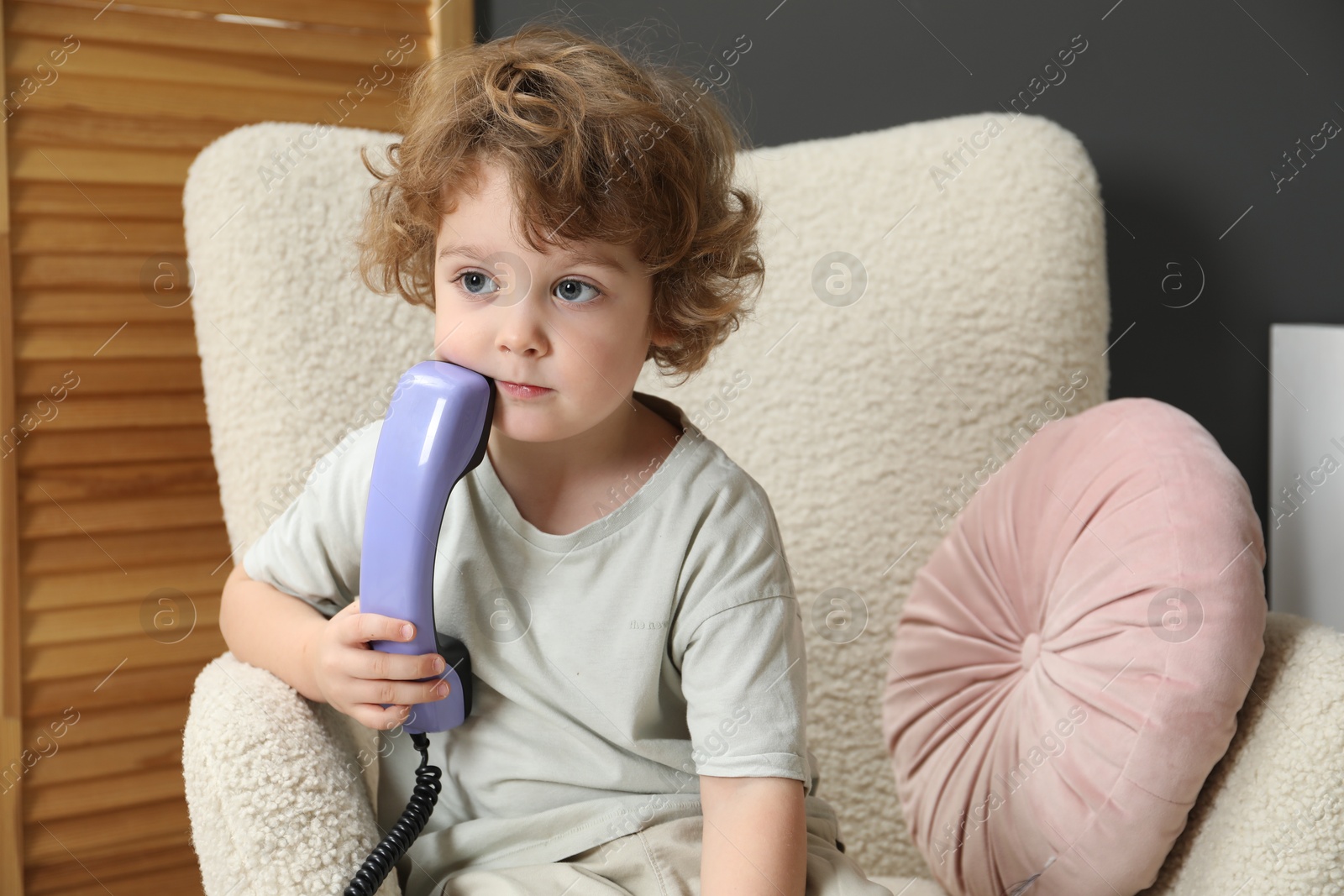 Photo of Cute little boy with telephone handset in armchair indoors