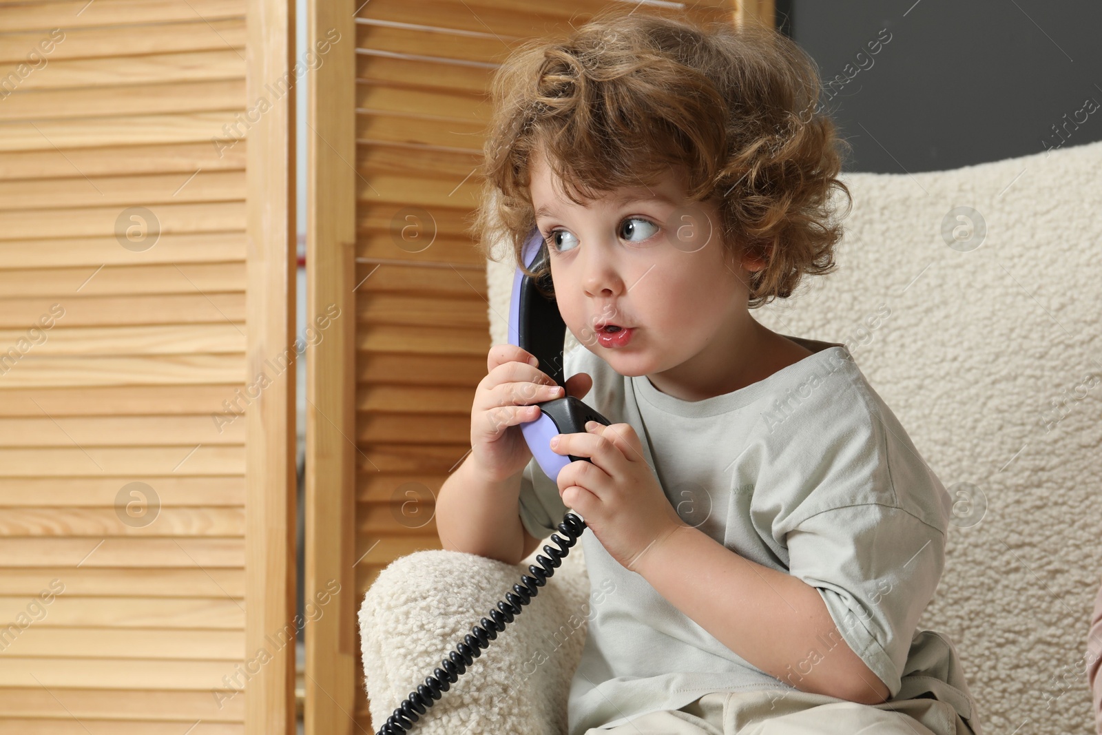 Photo of Cute little boy with telephone handset in armchair indoors, space for text