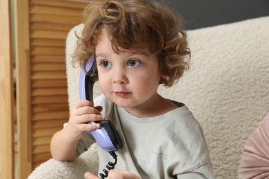 Cute little boy with telephone handset in armchair indoors