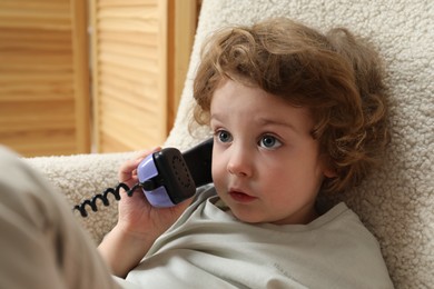 Photo of Cute little boy with telephone handset in armchair indoors