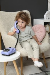 Photo of Cute little boy with telephone in armchair indoors