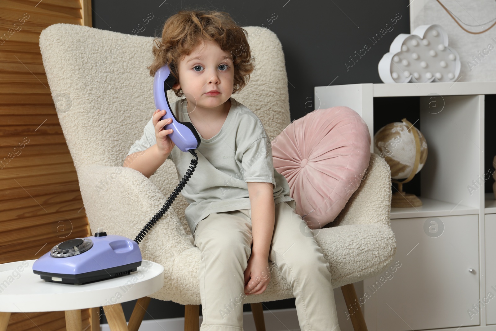 Photo of Cute little boy with telephone in armchair indoors