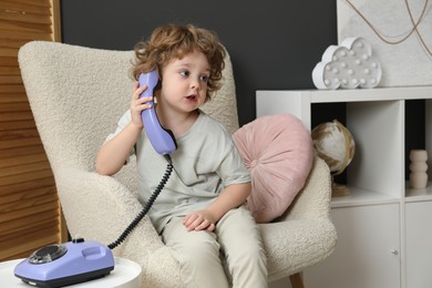 Photo of Cute little boy with telephone in armchair indoors