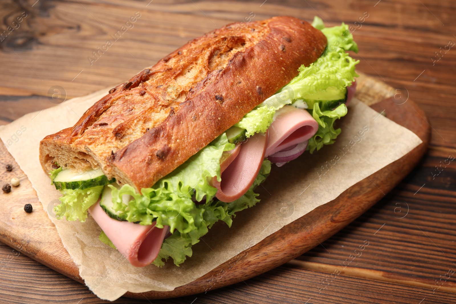 Photo of Delicious baguette sandwich with ham on wooden table, closeup