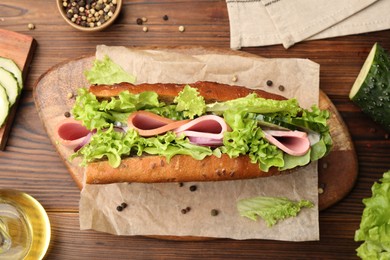 Photo of Delicious baguette sandwich with ham and ingredients on wooden table, flat lay