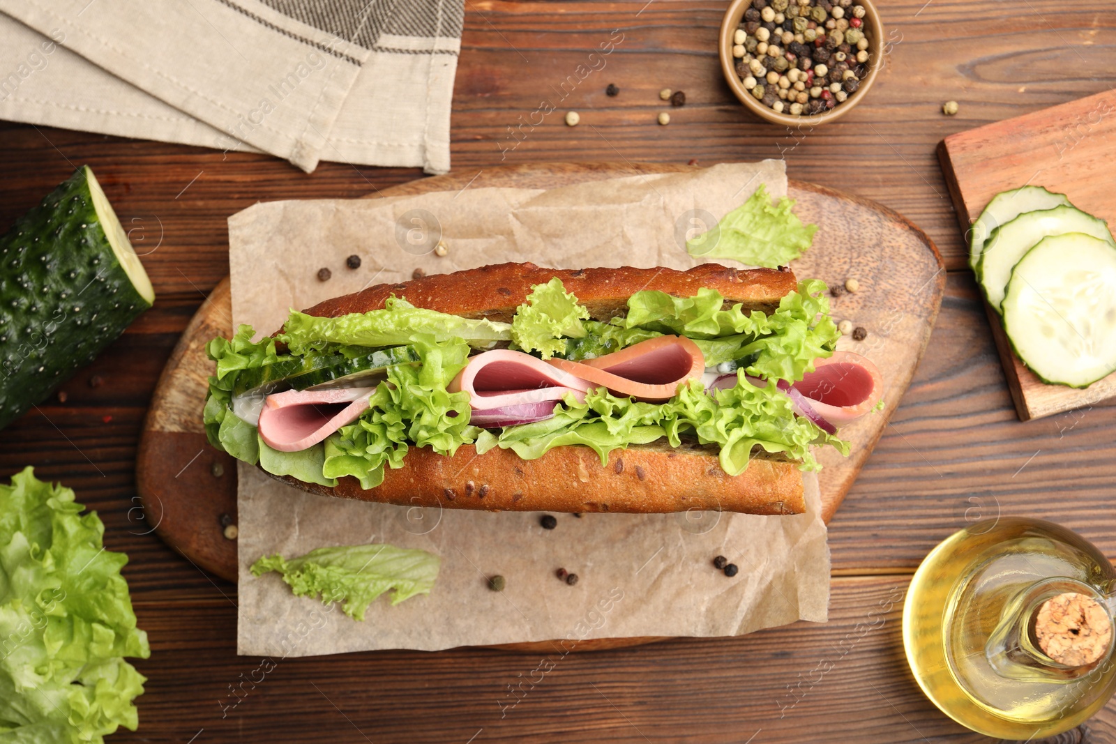 Photo of Delicious baguette sandwich with ham and ingredients on wooden table, flat lay