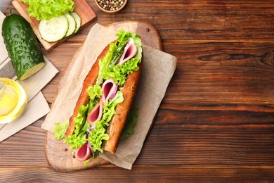 Photo of Delicious baguette sandwich with ham and ingredients on wooden table, flat lay. Space for text