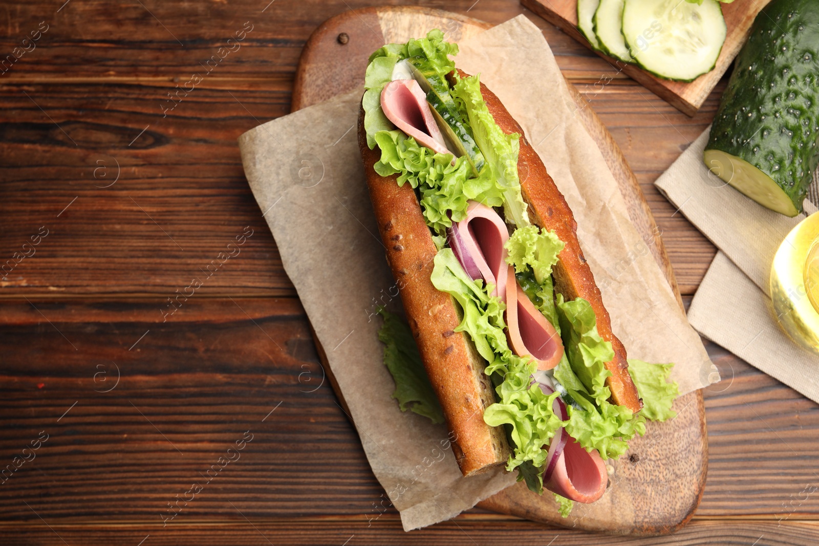 Photo of Delicious baguette sandwich with ham and ingredients on wooden table, flat lay. Space for text