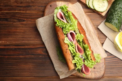 Photo of Delicious baguette sandwich with ham and ingredients on wooden table, flat lay. Space for text