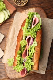 Photo of Delicious baguette sandwich with ham and ingredients on wooden table, flat lay