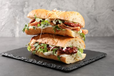 Photo of Halves of baguette sandwich with prosciutto and sun dried tomatoes on grey table