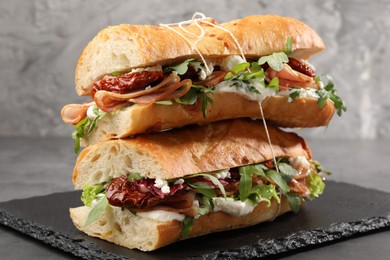 Photo of Halves of baguette sandwich with prosciutto and sun dried tomatoes on grey table, closeup