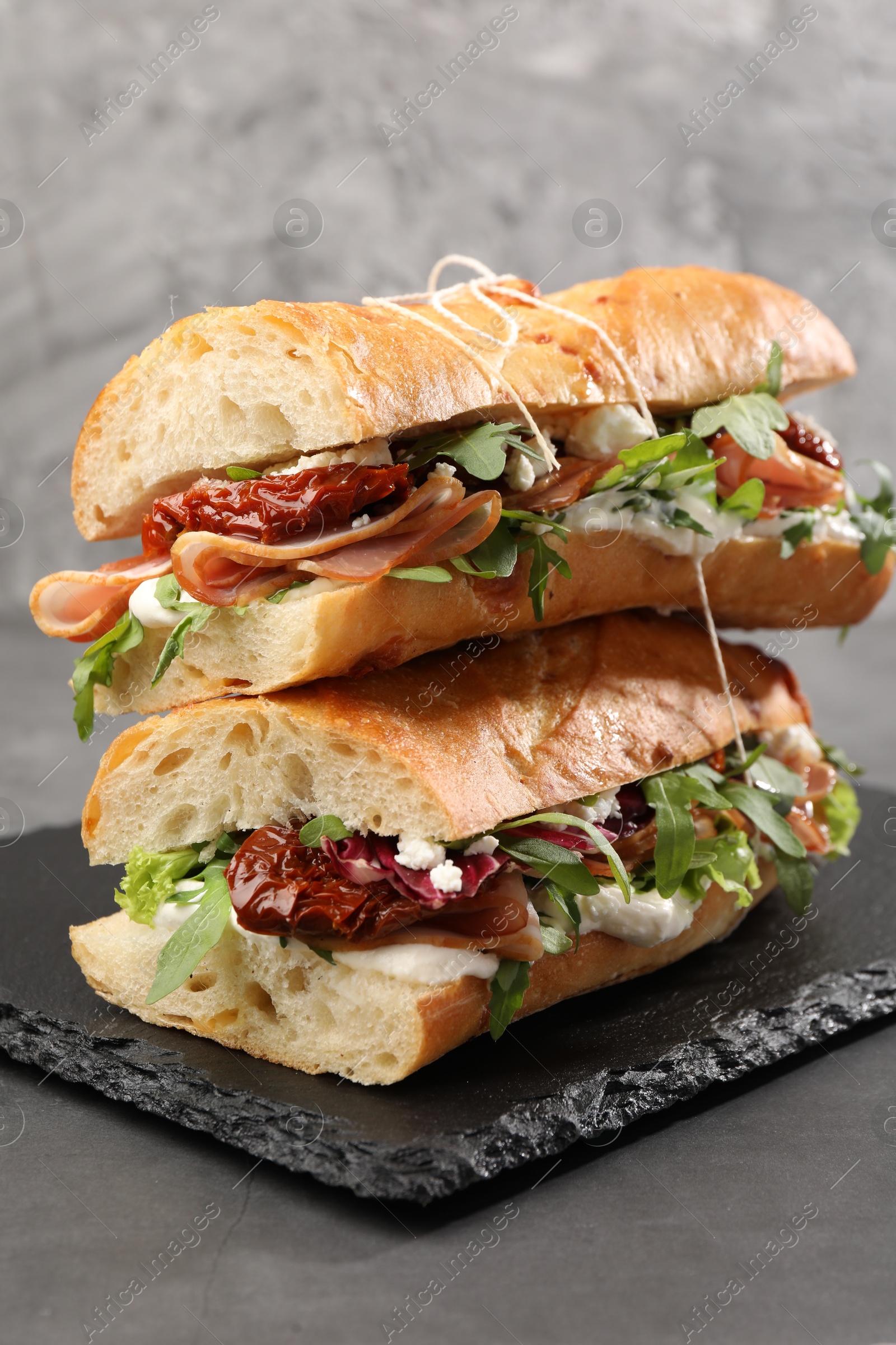 Photo of Halves of baguette sandwich with prosciutto and sun dried tomatoes on grey table, closeup