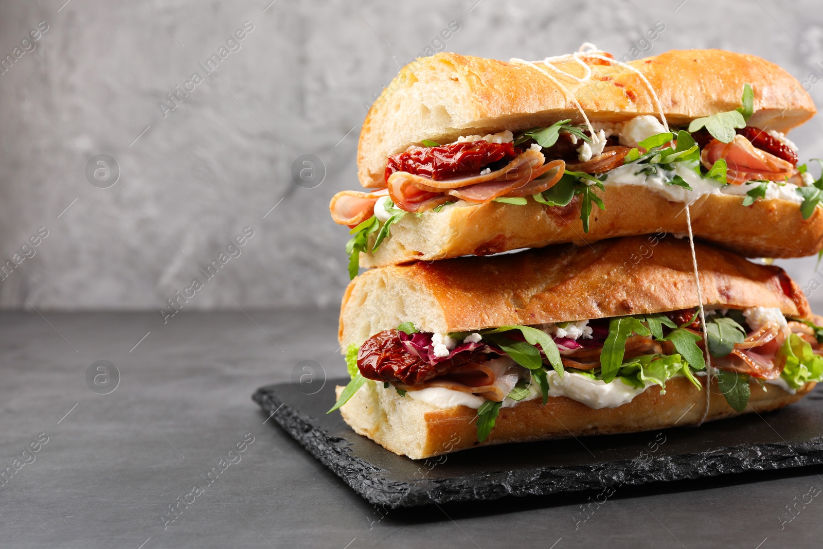 Photo of Halves of baguette sandwich with prosciutto and sun dried tomatoes on grey table, closeup. Space for text