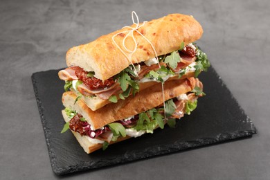 Photo of Halves of baguette sandwich with prosciutto and sun dried tomatoes on grey table