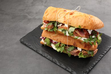 Photo of Halves of baguette sandwich with prosciutto and sun dried tomatoes on grey table