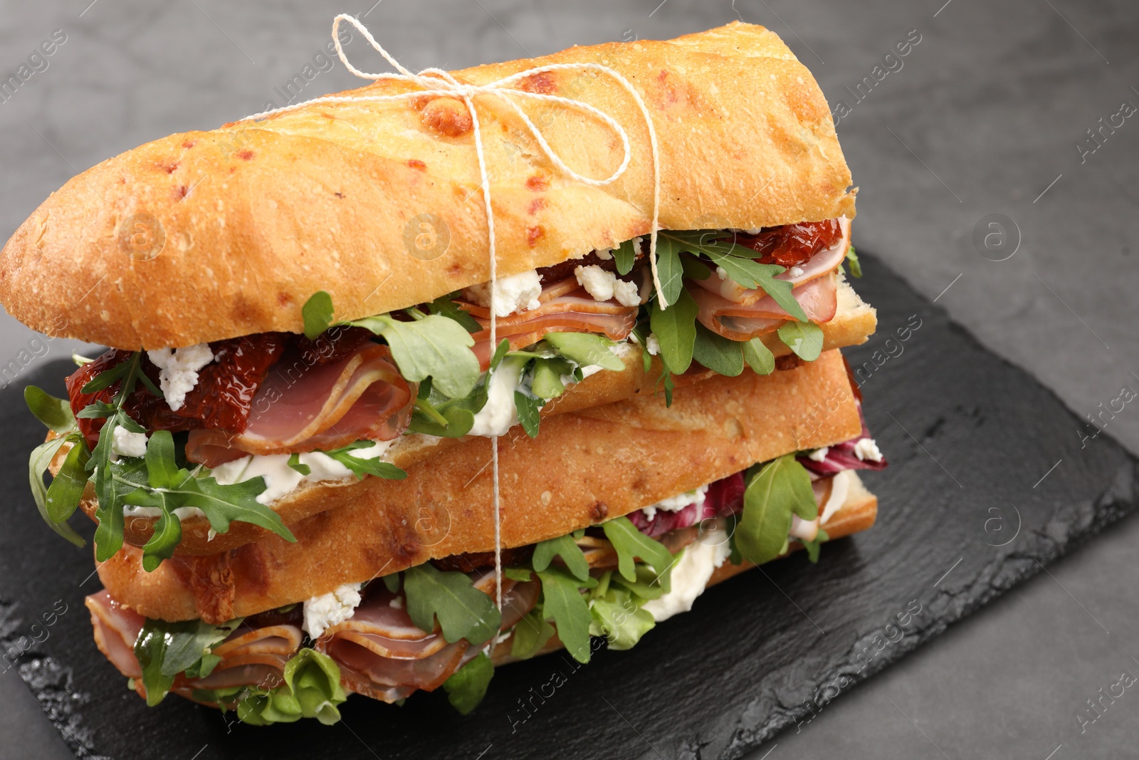 Photo of Halves of baguette sandwich with prosciutto and sun dried tomatoes on grey table, closeup