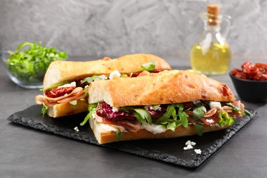 Photo of Halves of baguette sandwich with prosciutto and sun dried tomatoes on grey table, closeup