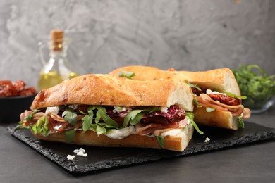 Photo of Halves of baguette sandwich with prosciutto and sun dried tomatoes on grey table, closeup