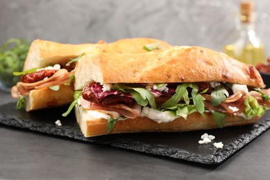 Photo of Halves of baguette sandwich with prosciutto and sun dried tomatoes on grey table, closeup