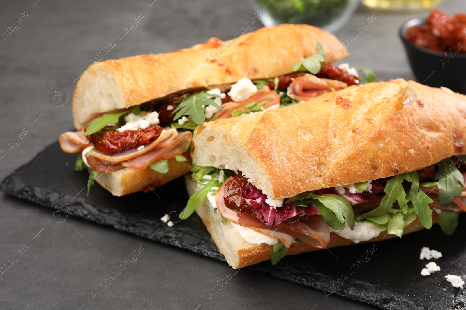 Photo of Halves of baguette sandwich with prosciutto and sun dried tomatoes on grey table, closeup