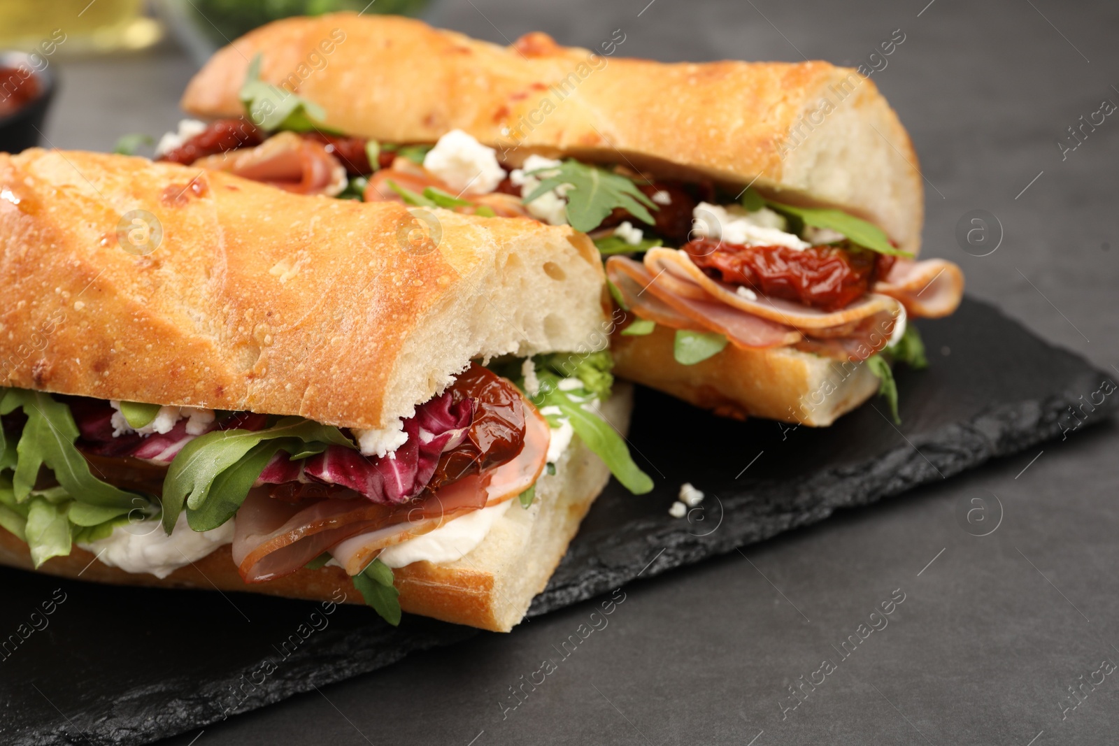 Photo of Halves of baguette sandwich with prosciutto and sun dried tomatoes on grey table, closeup