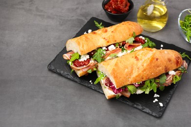 Photo of Halves of baguette sandwich with prosciutto and sun dried tomatoes on grey table