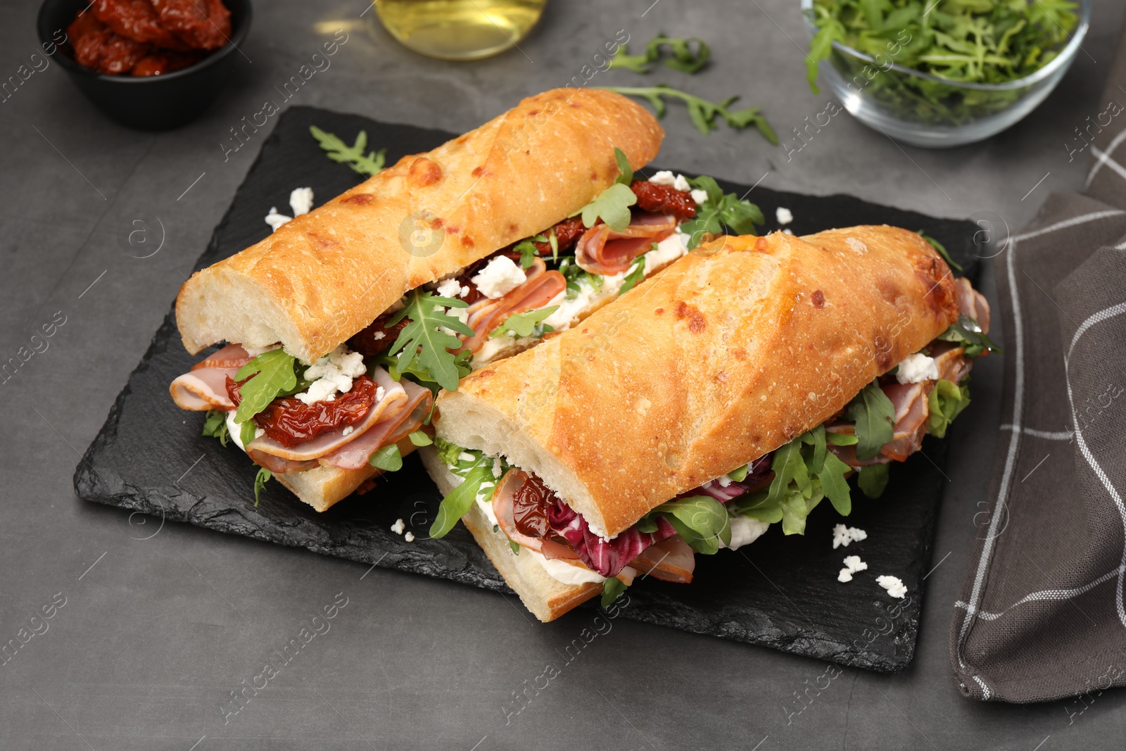 Photo of Halves of baguette sandwich with prosciutto and sun dried tomatoes on grey table