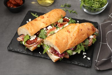 Photo of Halves of baguette sandwich with prosciutto and sun dried tomatoes on grey table