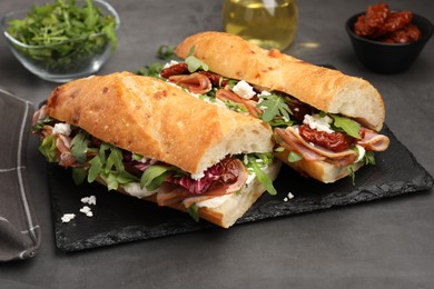 Photo of Halves of baguette sandwich with prosciutto and sun dried tomatoes on grey table