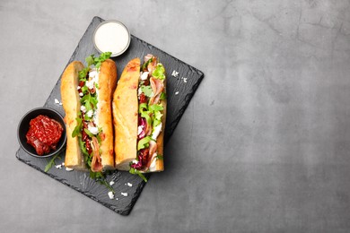 Photo of Halves of baguette sandwich with prosciutto and sun dried tomatoes served on grey table, top view. Space for text