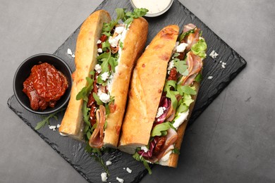 Photo of Halves of baguette sandwich with prosciutto and sun dried tomatoes served on grey table, top view