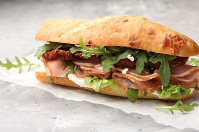 Photo of Baguette sandwich with ham and sun dried tomatoes on grey textured table, closeup