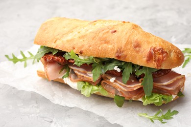 Photo of Baguette sandwich with ham and sun dried tomatoes on grey textured table, closeup