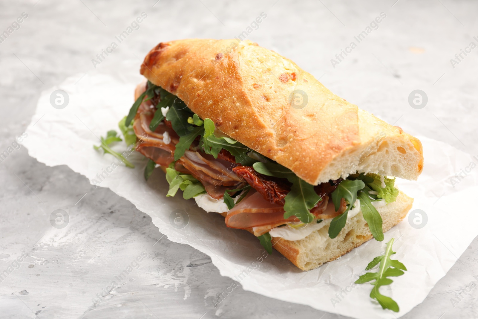 Photo of Baguette sandwich with ham and sun dried tomatoes on grey textured table, closeup