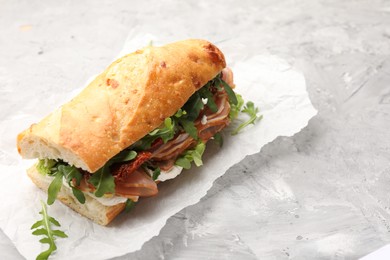 Photo of Baguette sandwich with ham and sun dried tomatoes on grey textured table, closeup