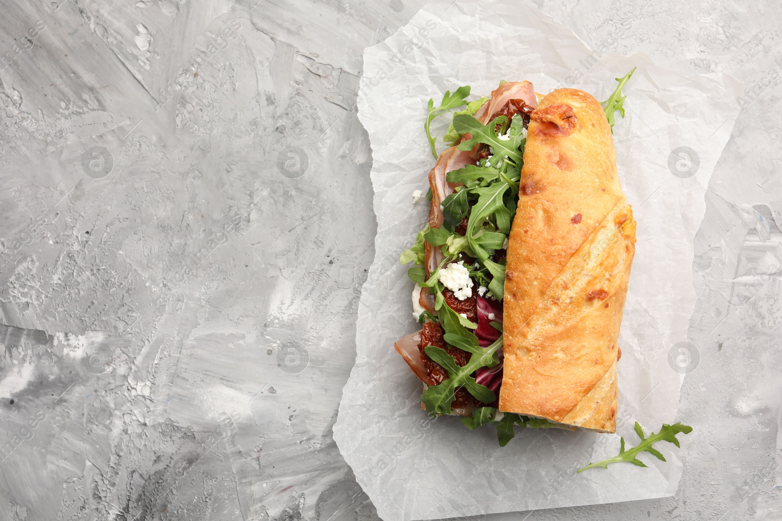 Photo of Baguette sandwich with ham and sun dried tomatoes on grey textured table, top view. Space for text